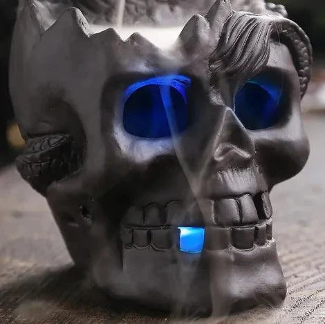 Skull-shaped backflow incense burner with LED light and cascading smoke effect.