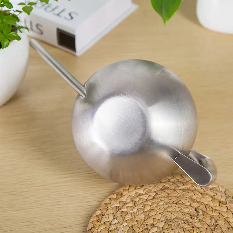 Stainless steel spherical watering can on wooden surface.